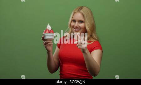 Junge Frau, die Erdbeereis in einer lebendigen Umgebung mit grünem Hintergrund genießt und Glück und Freude verkörpert. Stockfoto