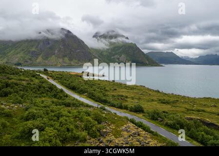 Aus der Vogelperspektive auf einer malerischen Straße in Lofoten, Norwegen, mit nebelbedeckten Bergen und Fjordlandschaft an einem bewölkten Sommertag. Stockfoto