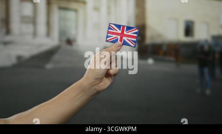 Mann mit gesticktem unions-Jack-Flaggenaufnäher in einer Straßenlandschaft im Freien, in der britisches Thema mit verschwommenem urbanem Hintergrund präsentiert wird. Stockfoto