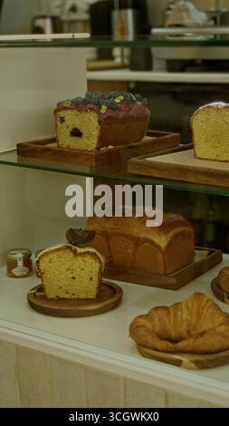 Verschiedene Gebäckstücke, darunter Brotkuchen und Croissants, werden auf Holztabletts in einem gemütlichen Restaurant präsentiert, in dem köstliche Backwaren im Innenbereich serviert werden. Stockfoto
