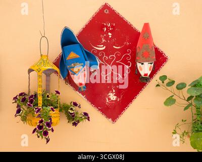 Alghero, Sassari, Sardinien, Italien. Auffällige Ausstellung von Blumen und Masken auf einer typischen pastellfarbenen Wand im Herzen der Altstadt. Stockfoto