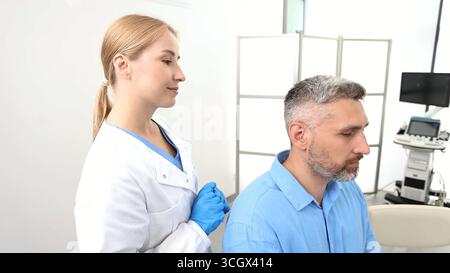 Erfahrene Ärztin, die hinter-dem-Ohr-Hörgerät an das Ohr des älteren Patienten anpasst, während der Sprechstunde in der audiologischen Klinik Stockfoto