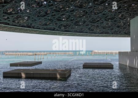 VAE - Abu Dhabi - Louvre Abu Dhabi Courtyard - Meeresbrise plaza, wo die Gitterkuppel einen zarten Lichtregen auf das Wasser sprengt Stockfoto