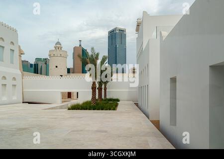 VAE - Abu Dhabi - Qasr Al Hosn Courtyard - Weiße Wände, Palmen und Wachtturm eingerahmt von der aufsteigenden Skyline der Innenstadt Stockfoto