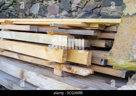 Eine detaillierte Aufnahme von verschiedenen Holzdielen, die an einer zerklüfteten Steinmauer gestapelt sind und die verschiedenen Farben und Körnungen des Holzes zeigen. Stockfoto