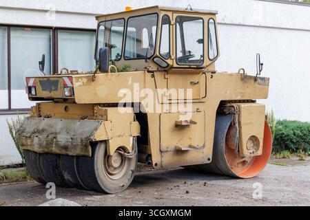 Eine alte, gelb-schwarze Straßenwalze mit breiter Trommel steht auf einer Straße vor einem weißen Gebäude. Stockfoto