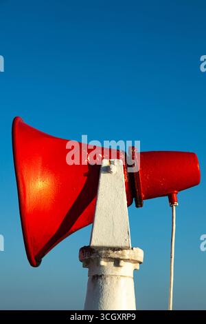 Ein rotes Schiffshorn ist auf einem Stahlgestell gegen einen blauen Himmel befestigt. Stockfoto
