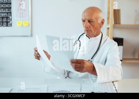 Seriöser Oberarzt, der Papiere macht und medizinische Dokumente überprüft, die in seiner Arztpraxis sitzen. DOC-Analyse der Patientendiagnostik im Krankenhaus. Spac kopieren Stockfoto