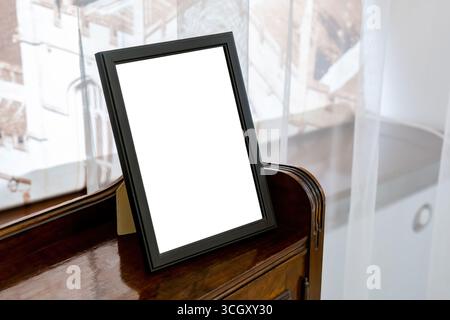 Einfacher schwarzer Bildrahmen mit einem Ständer auf einem Holzregal zu Hause, leerer weißer Raum in der Mockup-Vorlage für Personenporträt-Foto, Stockfoto