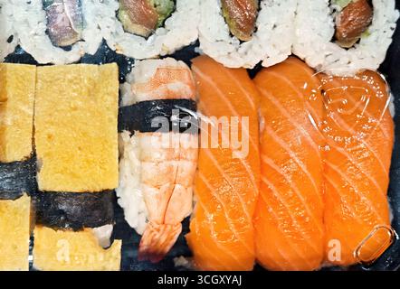 Sushi-Set in einer Plastikkiste zum Mitnehmen mit Lachs-Nigiri, Garnelen-ebi, Tamago- und Maki-Brötchen, Reis und Nori, sichtbare Draufsicht durch die durchsichtige Verpackung Stockfoto