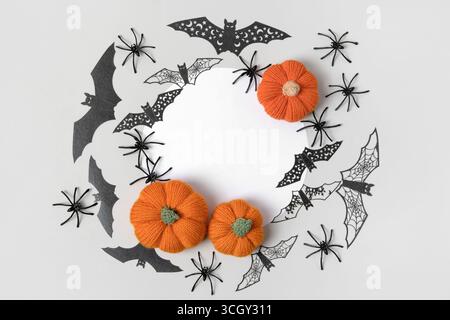 Halloween-Komposition aus gestrickten orangefarbenen Kürbissen, schwarzen Spinnweben und Spinnen und Fledermäusen mit einem runden weißen Textfeld. Handgefertigtes Strickspielzeug für Kinder und Dekoration für das Ferienhaus. Stockfoto