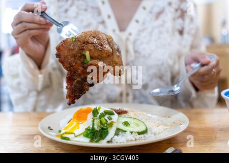 Traditioneller vietnamesischer Bruchreis oder com Tam mit gegrilltem Schweinekotelett, Spiegelei, Gurke und Zwiebelöl. Beliebtes Street Food in Saigon und authentisches Stockfoto