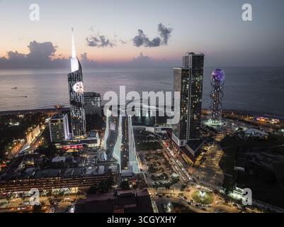 Blick aus der Vogelperspektive auf das beleuchtete Stadtbild mit dem alphabetischen Turm und modernen Wolkenkratzern im Kontrast zum ruhigen Dämmerungsmeer Batumi, Adjara, Georgia. Stockfoto