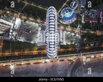 Aus der Vogelperspektive auf ein elegantes, modernes Hochhaus, das lange Schatten über den Strand wirft, mit dem türkisfarbenen Pool in der Nähe, Batumi, Adjara, Georgia. Stockfoto