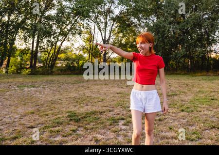 Junge Frau, die während des Sonnenuntergangs in einen Park zeigt und ruft Stockfoto