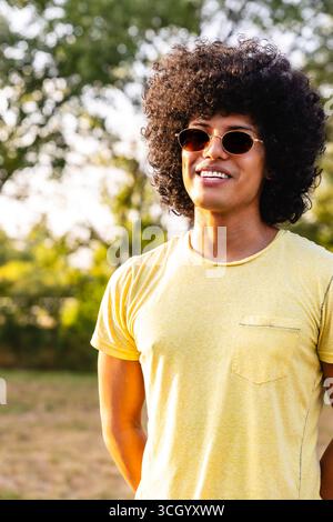 Junger Mann mit Sonnenbrille und Afro-Frisur, der den Sommer im Park genießt Stockfoto