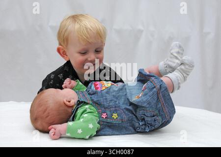 Ein zweijähriger Junge, der seine kleine Schwester ansieht. Stockfoto