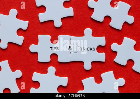 Symbol für Tipps und Tricks. Unter den verstreuten Puzzleteilen bilden zwei miteinander verbundene die Worte „Tipps und Tricks“. Geschäftskonzept. Auch hilfreiche Tricks Stockfoto