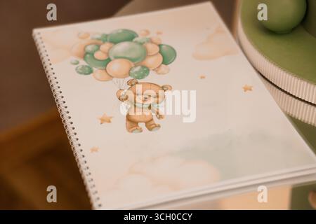 Ein bezauberndes Baby-Scrapbook mit einem niedlichen Teddybären, der Ballons hält, wird gezeigt, ideal für erste Erinnerungen. Sanfte Pastellfarben und Kinderzimmer. p Stockfoto