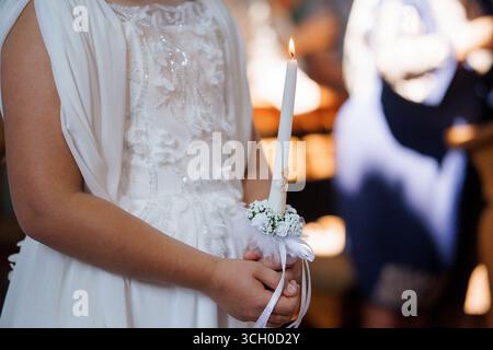 Eine schöne Braut hält zärtlich eine brennende Kerze, die mit weißen Bändern und zarten Blumen während einer orthodoxen christlichen Hochzeitszeremonie, Chu, verziert ist Stockfoto