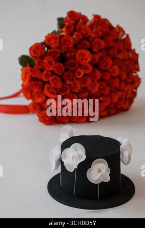 Ein üppiger Blumenstrauß aus leuchtend roten Rosen wird mit einem eleganten schwarzen Hut-Kuchen mit weißer Blüte kombiniert, der ein perfektes Geschenk für ein besonderes Geschenk darstellt Stockfoto