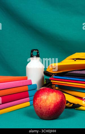 Back-to-School-Konzept mit bunten Büchern, gelbem Rucksack, rotem Apfel und wiederverwendbarer Wasserflasche für einen gesunden Lebensstil Stockfoto