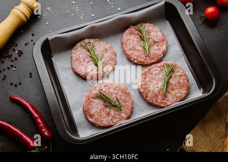 Vier rohe Schweinebraten mit Rosmarin zum Grillen, Blick von oben mit Zutaten Stockfoto