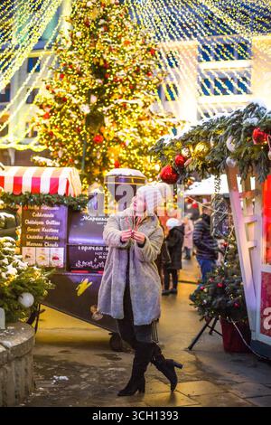 moskau, russland, 12.01.2020 Eine glückliche Frau steht mit Zuckerrohrherzen auf einem hell erleuchteten Weihnachtsmarkt. Festliche Feiertage. Stockfoto