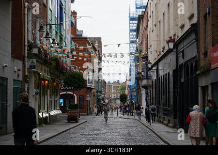 Eine enge, kopfsteingepflasterte Straße im Stadtzentrum Dublins ist mit irischen Fahnen und Fahnen geschmückt, auf der die Menschen entlang der Straße laufen. Stockfoto