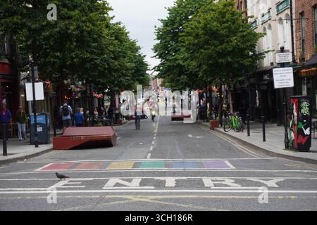Ein Weitwinkelfoto einer lebhaften Straße in Dublin mit dem Schild „Entry“ und einem Regenbogenübergang mit Fußgängern im Hintergrund. Stockfoto