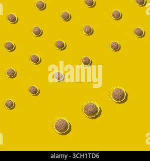 Ein stilles Leben über dem Kopf mit Schokoladentrüffelbonbons in Pappbechern, platziert in ordentlichen diagonalen Reihen auf einer lebhaften gelben Oberfläche mit verspieltem Minus Stockfoto
