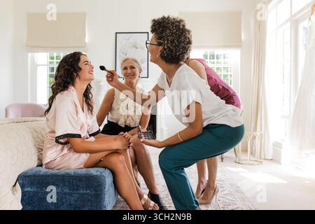 Braut wird geschminkt, während Familienmitglieder sich zu Hause fröhlich unterhalten Stockfoto