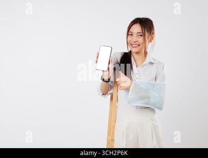 Verletzte asiatische Frau mit gebrochenem Arm, in einem Gips, das Telefon hält, benutzt mobile Unterstützung Stockfoto