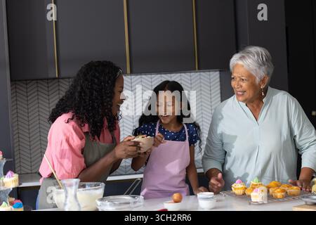 Zusammen Cupcakes backen, drei Generationen von Frauen lächeln und die Zeit der Familie teilen Stockfoto