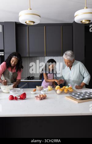 Drei Generationen backen gemeinsam Cupcakes in moderner Küche und genießen die Familienzeit Stockfoto