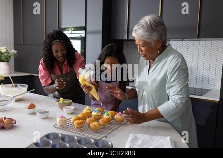 Die Dekoration von Cupcakes in der modernen Küche, drei Generationen, die fröhliche Momente miteinander teilen Stockfoto