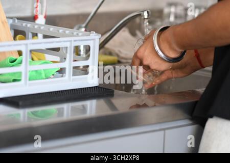 Cremona, Italien - 21. Juli 2025 Nahaufnahme der Hände, die Glaswaren unter fließendem Leitungswasser in einem modernen Spülbecken mit Geschirrablage in der Nähe waschen Stockfoto