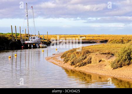 Ein kleines Boot ruht ruhig an einem hölzernen Steg am Fluss und spiegelt sich im ruhigen Wasser unter Frühlingsgrün. Stockfoto
