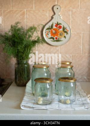 Ein Haufen Dill, Glasgläser und Kappen, bereit für hausgemachte Konfitüren in einer gemütlichen Küche mit Petrykivka-Blumendekor Stockfoto