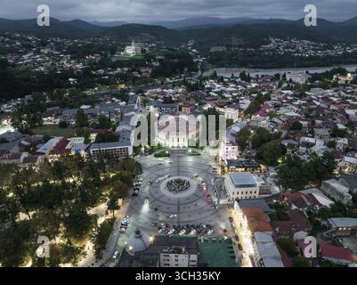 Der beleuchtete Colchis-Brunnen und die Semenowski-Kirche stehen aus der Vogelperspektive vor der dunklen, bergigen Kulisse, Kutaissi, Imereti, Georgien. Stockfoto