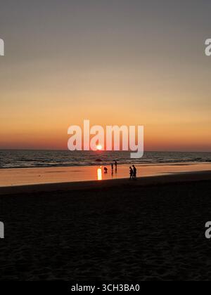 Silhouetten von Menschen, die während des Sonnenuntergangs über dem Meer am Sandstrand in Chipiona, einer Küstenstadt in Andalusien, Spanien, spazieren und spielen Stockfoto
