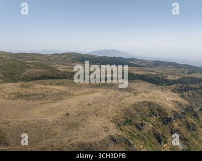 Aus der Vogelperspektive eine zerklüftete Landschaft mit trockenen Gräsern und karger Vegetation, die zum entfernten, trüben Gipfel des Mount Aragats, Mount Aragats, Provinz Shirak, Armenien führt. Stockfoto