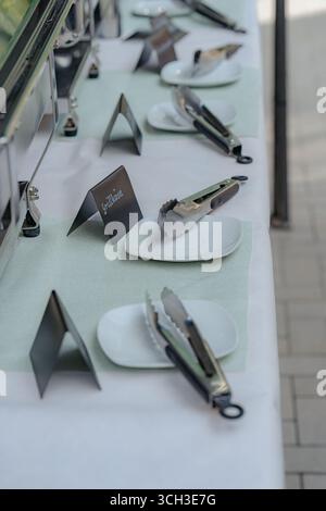 Nahaufnahme eines für Gäste zubereiteten Buffettisches mit weißen quadratischen Tellern, Servierzangen und schwarzen Lebensmitteletiketten. Elegantes Catering-Setup für Stockfoto
