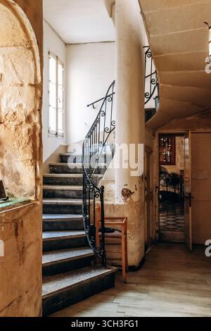 Eine altmodische Steintreppe mit verzierten schwarzen schmiedeeisernen Geländern in einem historischen Restaurant in Birgu, das authentische maltesische Architektur zeigt Stockfoto