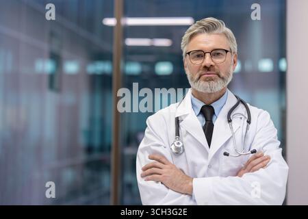 Erfahrener männlicher Arzt in professioneller Kleidung, der selbstbewusst in einer modernen Gesundheitseinrichtung steht. Stockfoto