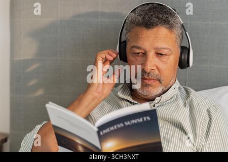 Ein älterer Mann, der sich im Bett entspannt, Musik hört und Bücher liest Stockfoto