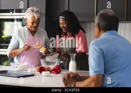 Ältere Mutter und Erwachsene Tochter backen in der Küche, während Vater zusieht, zu Hause Stockfoto