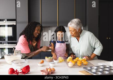 Drei glückliche Generationen backen, lächeln und dekorieren Cupcakes in der modernen Küche, zu Hause Stockfoto