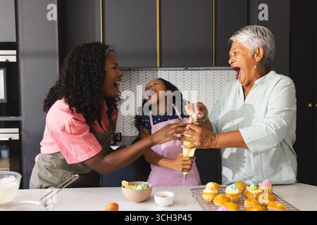 Cupcakes backen, drei glückliche Generationen lachen und knüpfen in der Küche, zu Hause Stockfoto