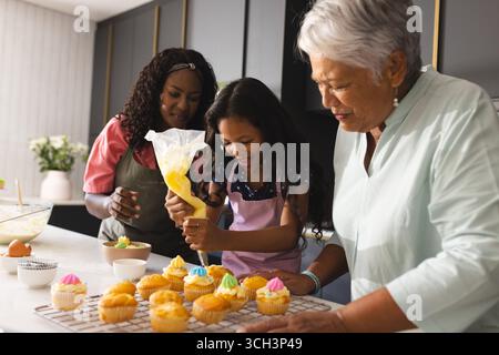 Drei glückliche Generationen, die Cupcakes dekorieren, genießen das Backen in der modernen Küche, zu Hause Stockfoto